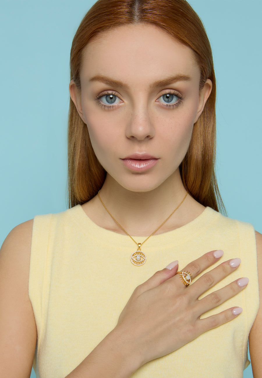 Mujer pelirroja con top amarillo luciendo un collar dorado con colgante de ojo turco con perla central y circonitas blancas, junto a un anillo a juego de Lavani Jewels.