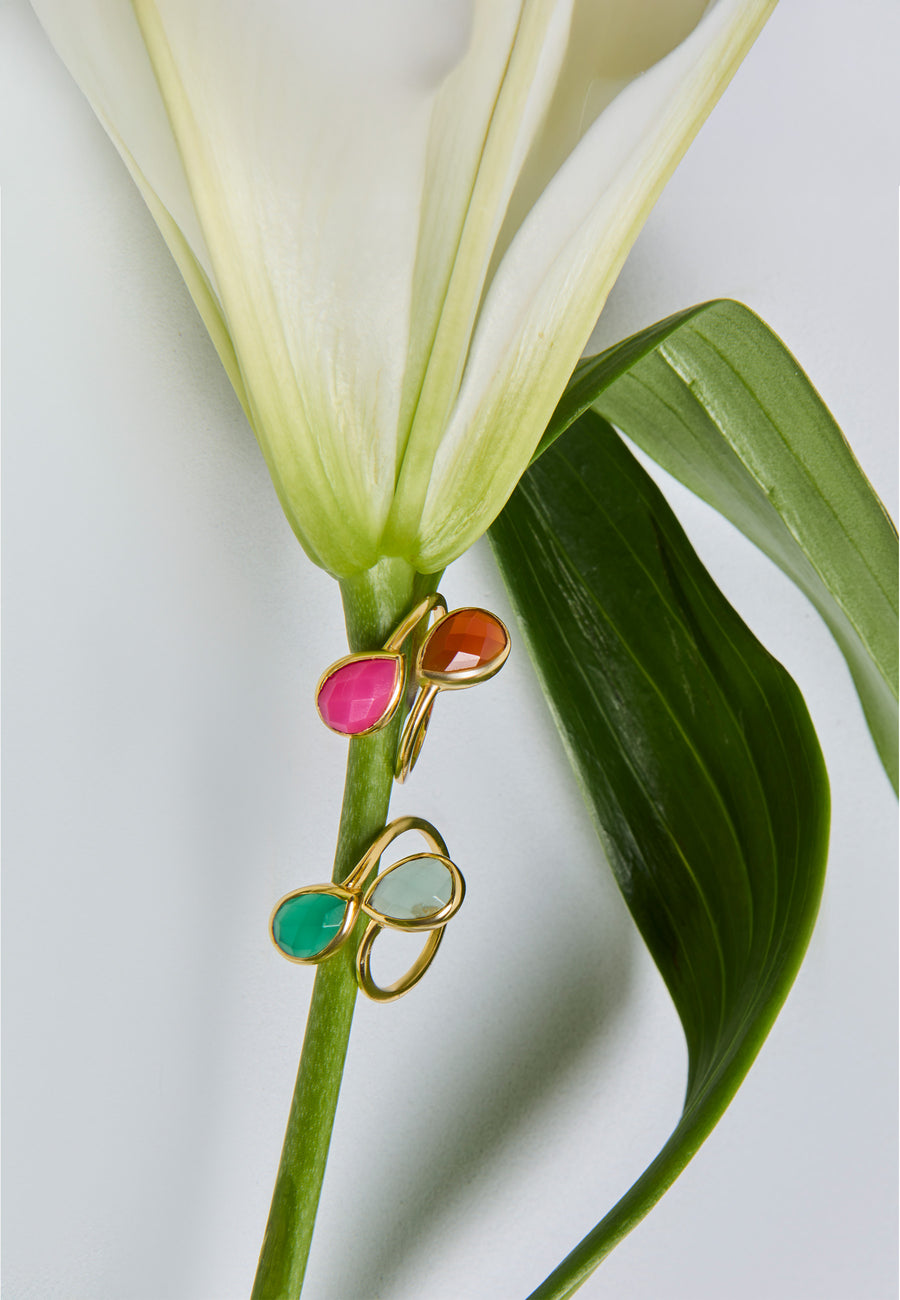 Anillos Aura dorados con piedras en fucsia, naranja, verde y menta sobre flor blanca. Joyería moderna y colorida para invitadas.