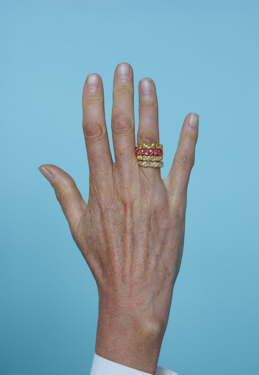 Mano luciendo varios anillos dorados Birthstone de Lavani Jewels, cada uno con piedras de nacimiento de diferentes colores.