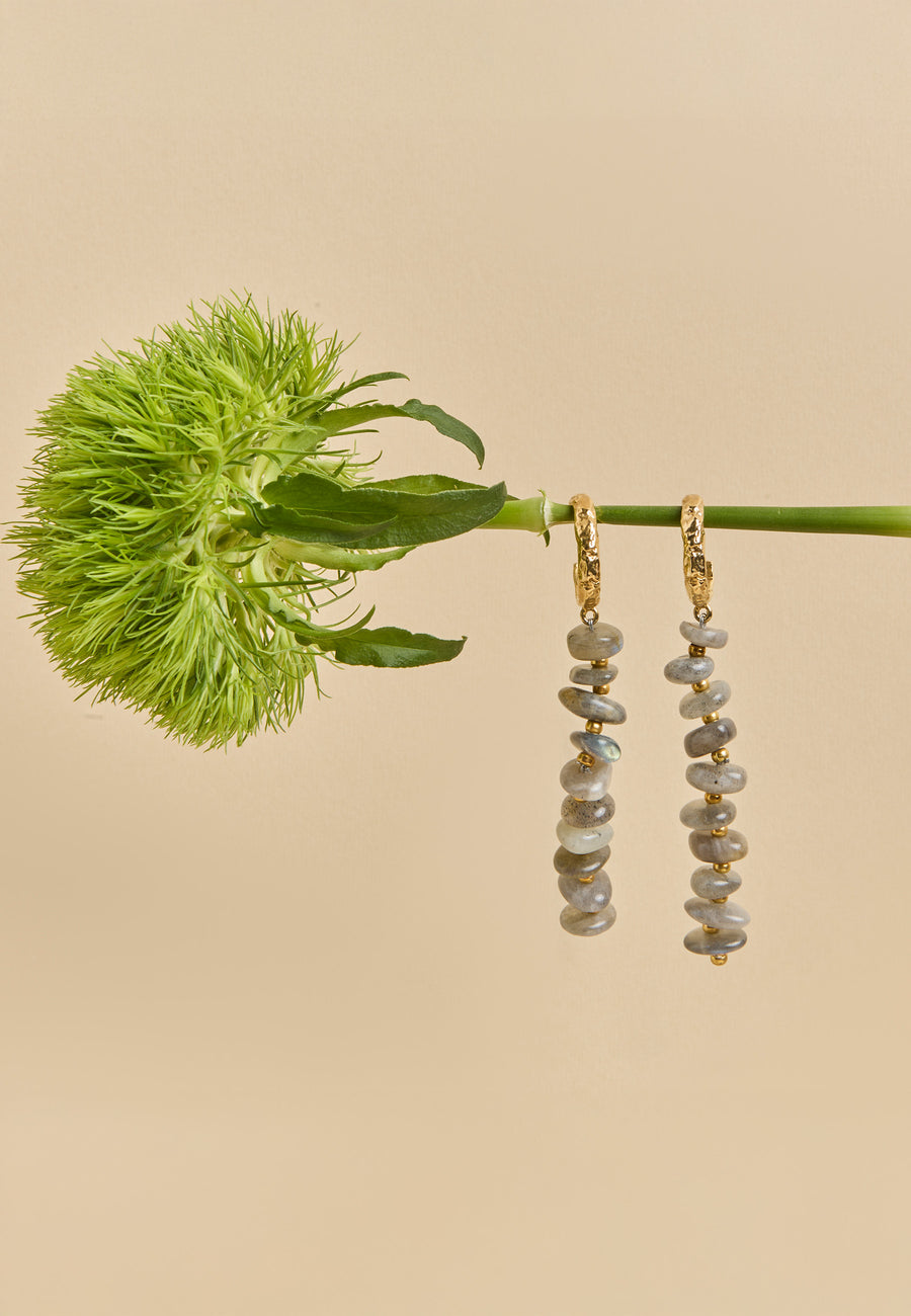 Aros Mizu Gris largos con cuentas grisáceas y doradas colgando de una flor verde exótica, joyería contemporánea de Lavani Jewels.