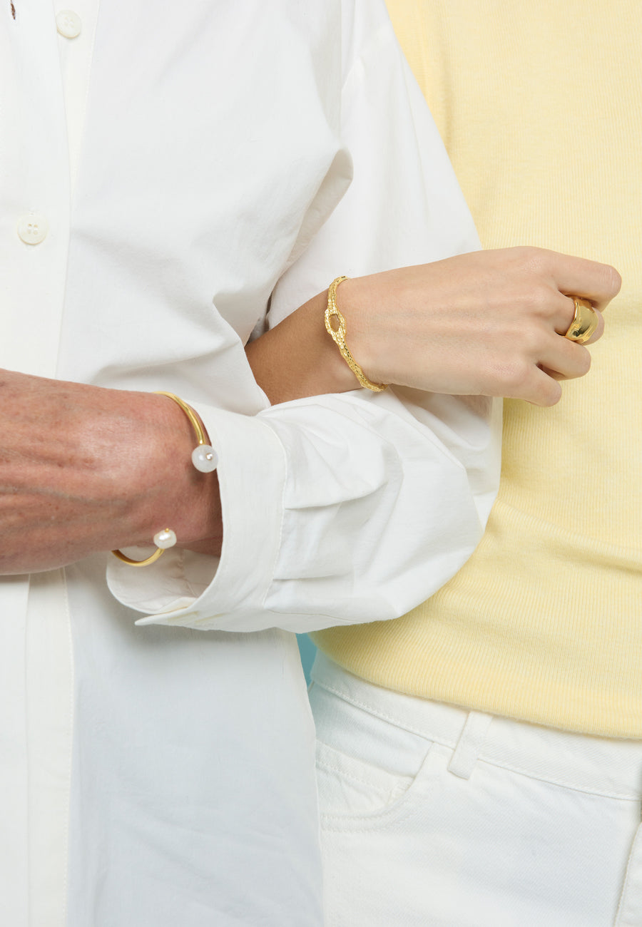 Primer plano de dos mujeres entrelazando brazos, una luce el brazalete dorado Rhea con perlas de Lavani Jewels y la otra un brazalete dorado texturizado.