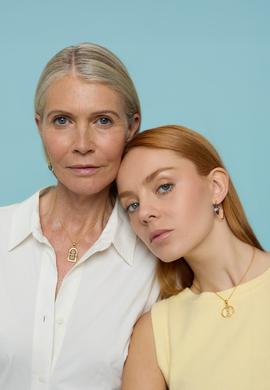 Mujer mayor y joven pelirroja posando juntas. La mujer joven lleva un collar dorado con colgante de infinito giratorio de Lavani Jewels. Día de la Madre.