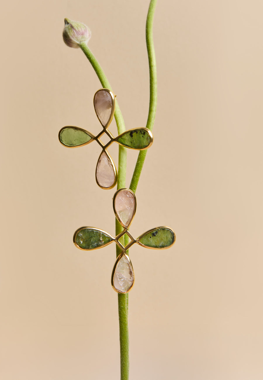 Pendientes Cruz Namasté de Lavani Jewels con piedras de cuarzo rosa y verde, dispuestos sobre una ramita natural.