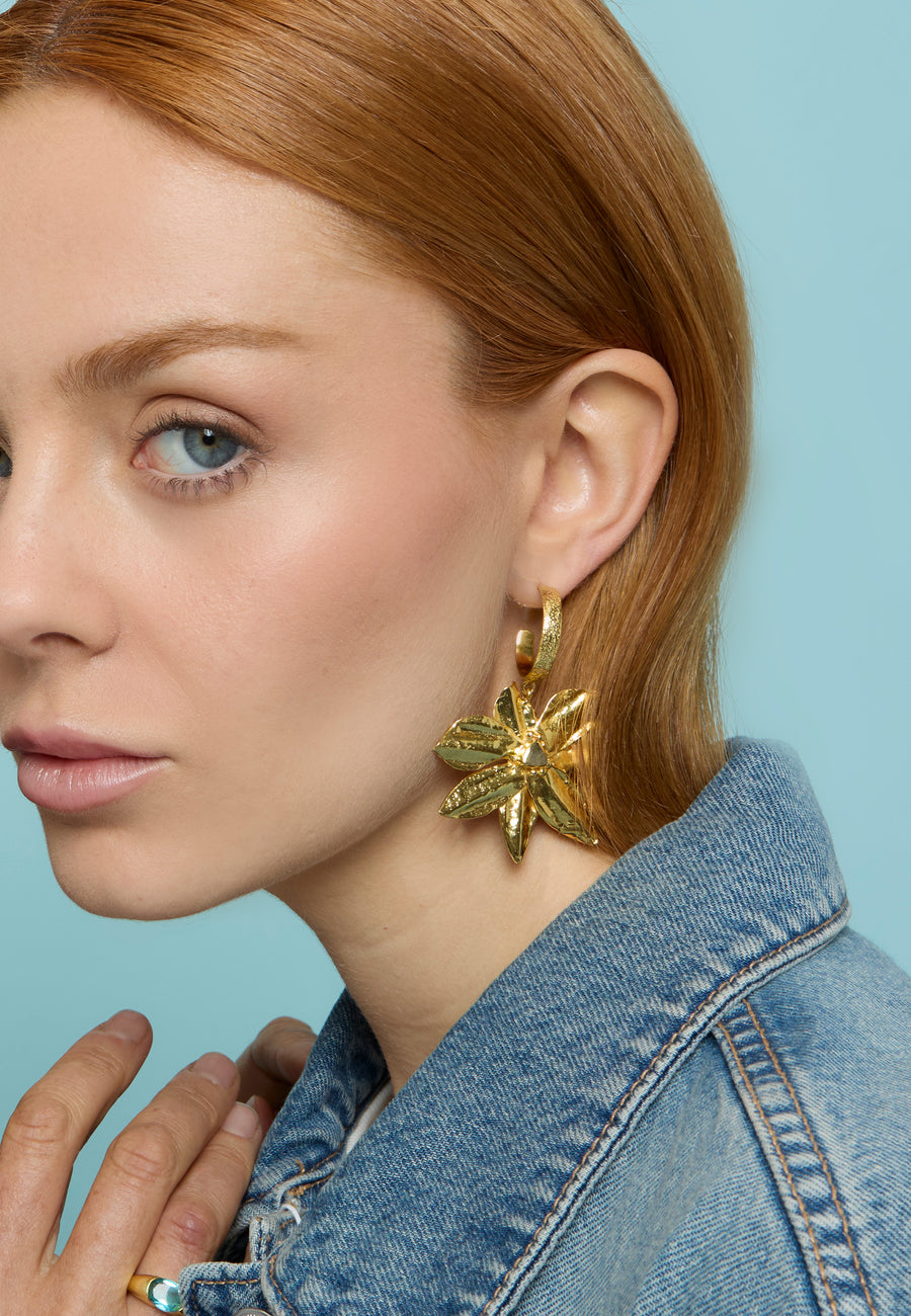 Mujer pelirroja con chaqueta vaquera luciendo los pendientes dorados Flor de Loto de Lavani Jewels, en forma de flor grande con textura metálica brillante.