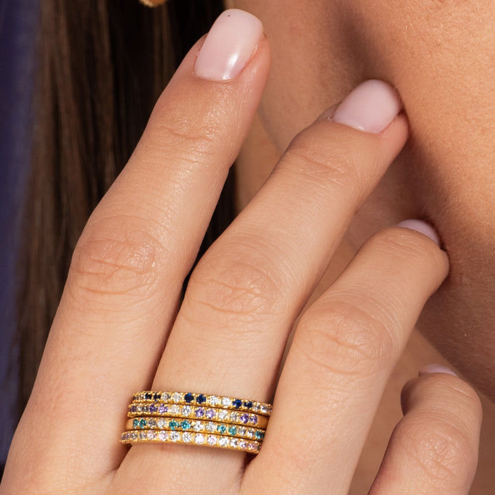 Mano de mujer con juego de 4 anillos finos decorados con circonitas de colores y con un baño de oro certificado.