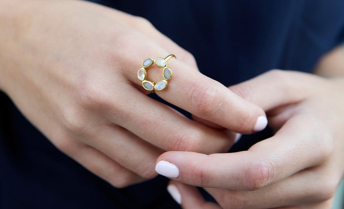 Anillo circular dorado con piedras naturales en tonos suaves, diseño floral minimalista.
