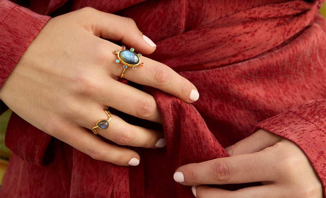 Anillos dorados con piedras naturales de muchos colores sobre fondo rojo, joyería elegante y llamativa.