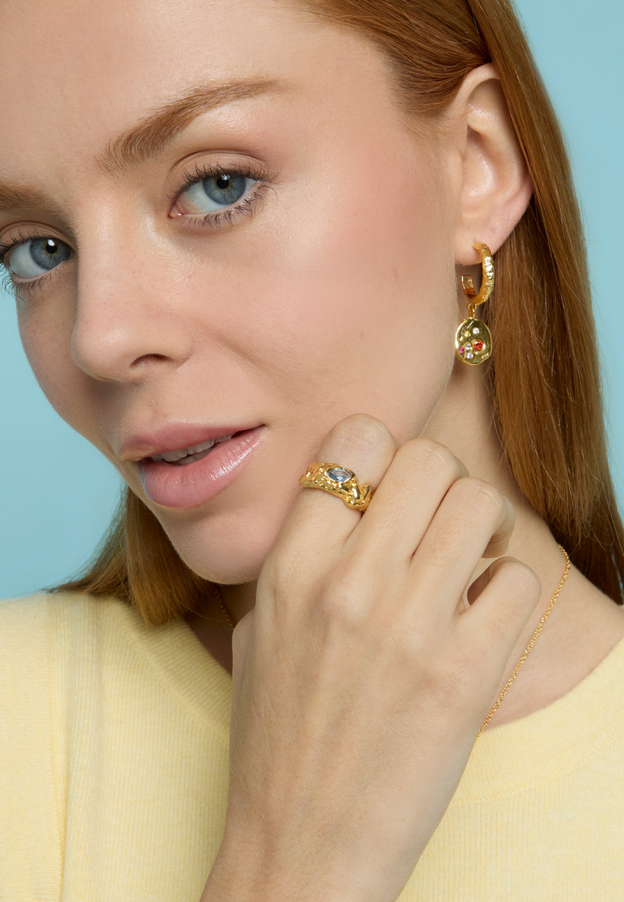 Mujer pelirroja con suéter amarillo luciendo los aros Sadie Coin con colgantes de moneda bañados en oro de 18k, combinados con un anillo artesanal dorado con piedra aguamarina de Lavani Jewels.