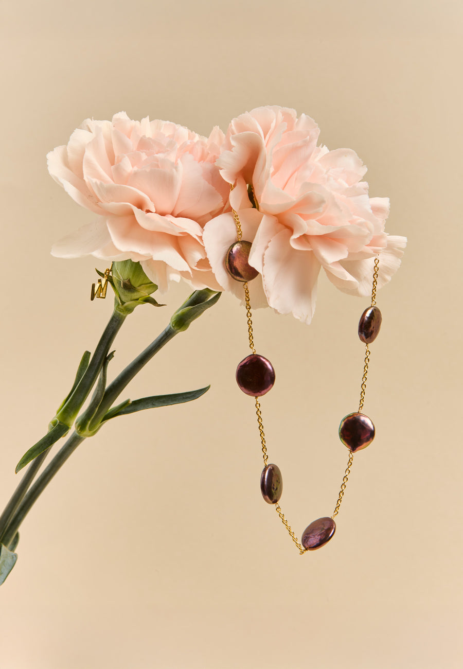 Choker de perla gris Siena de Lavani Jewels colgado sobre claveles rosa empolvado, ideal para una novia que busca un toque único y moderno.
