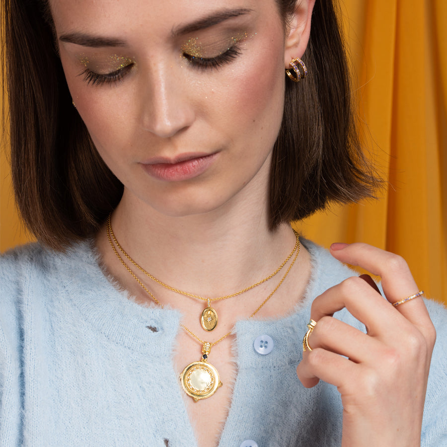 Chica lleva un colgante de moneda con piedras naturales colgada de una fina cadena dorada.