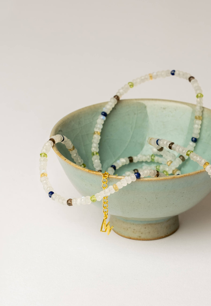 Collar de Piedra Luna de colores hecho con cuentas de la piedra Luna blanca dentro de un cuenco turquesa sobre fondo blanco