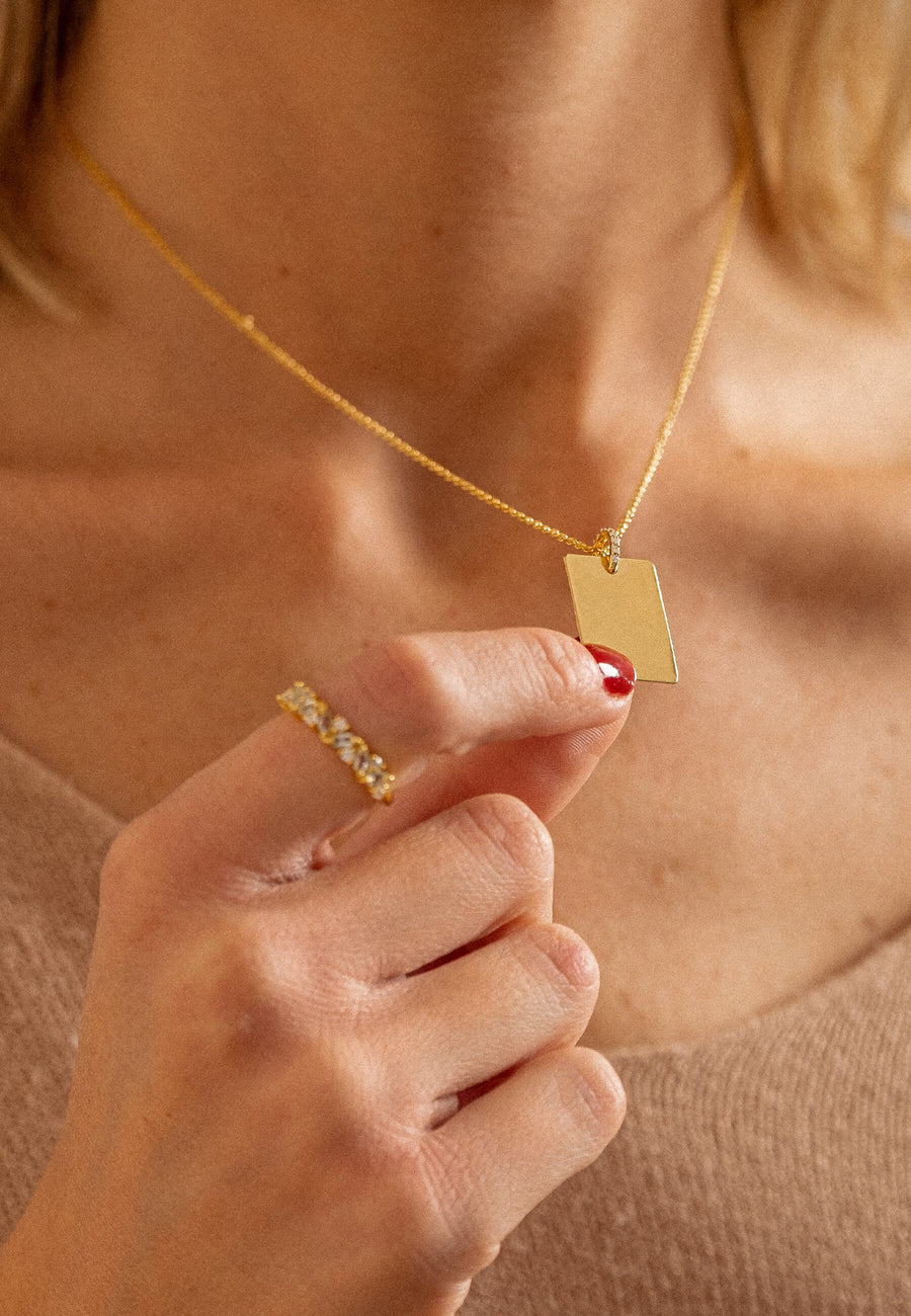 Mujer cujetando el colgante rectangular dorado grabado de Lavani Jewels con circonitas
